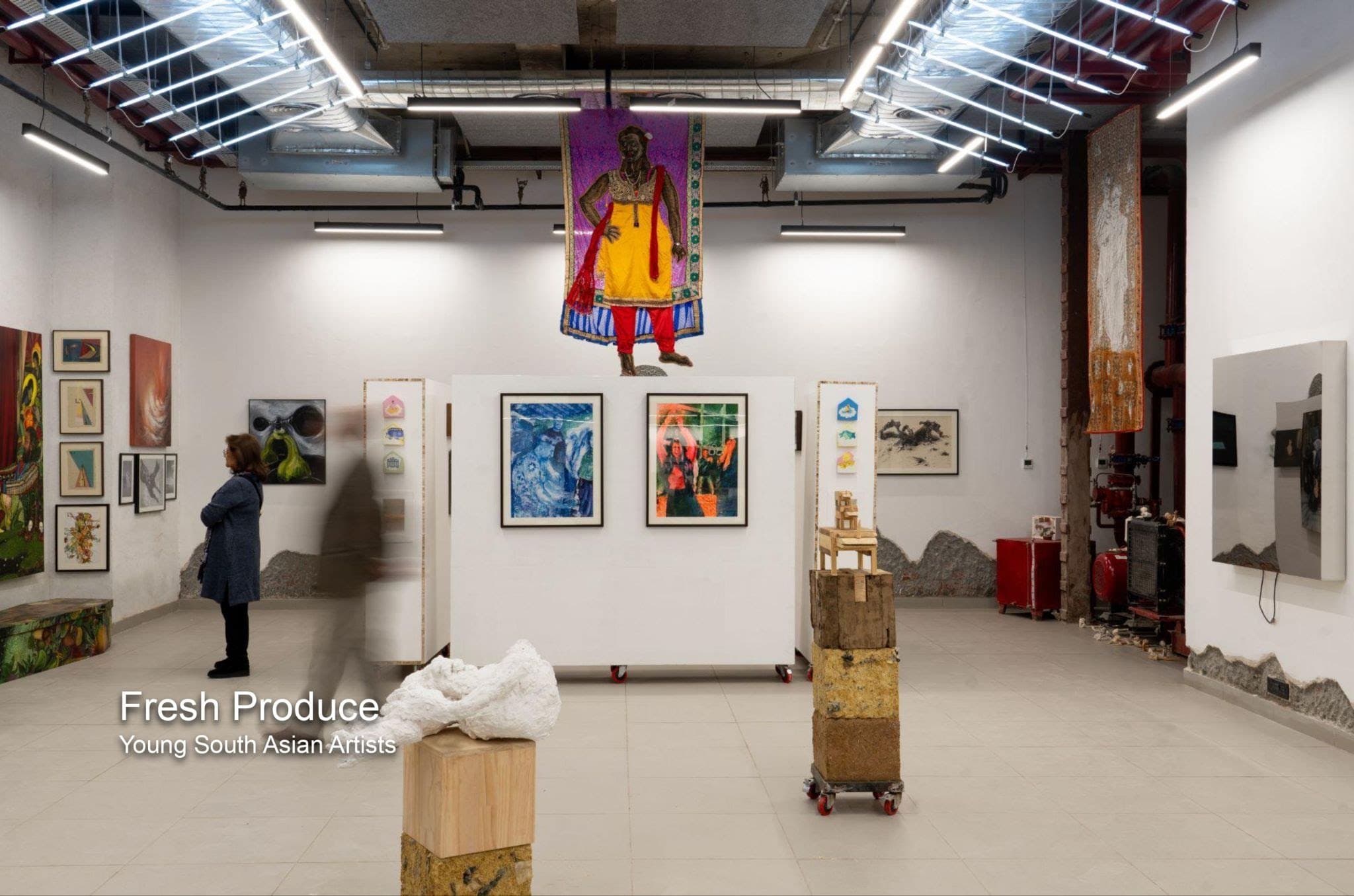 The gallery at Method Delhi with framed works on white walls and a textile figure suspended from the ceiling.