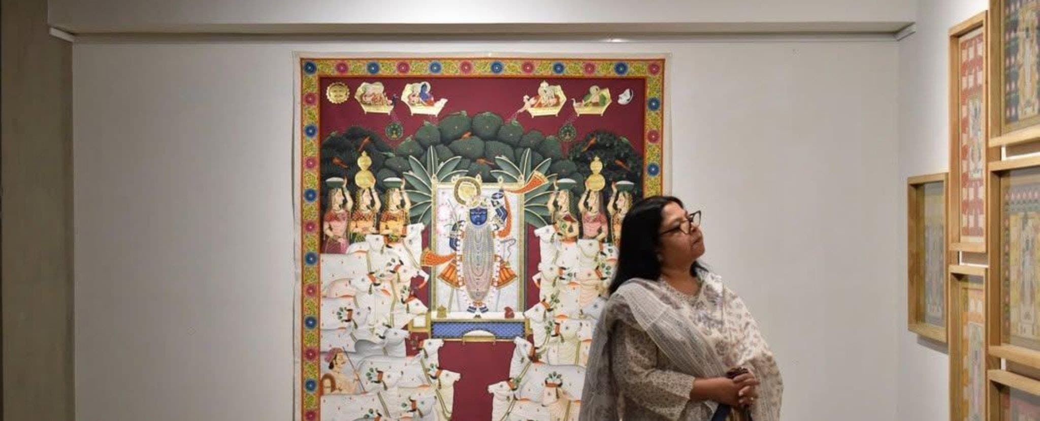 A visitor looking up at a large red-bordered Pichwai painting.