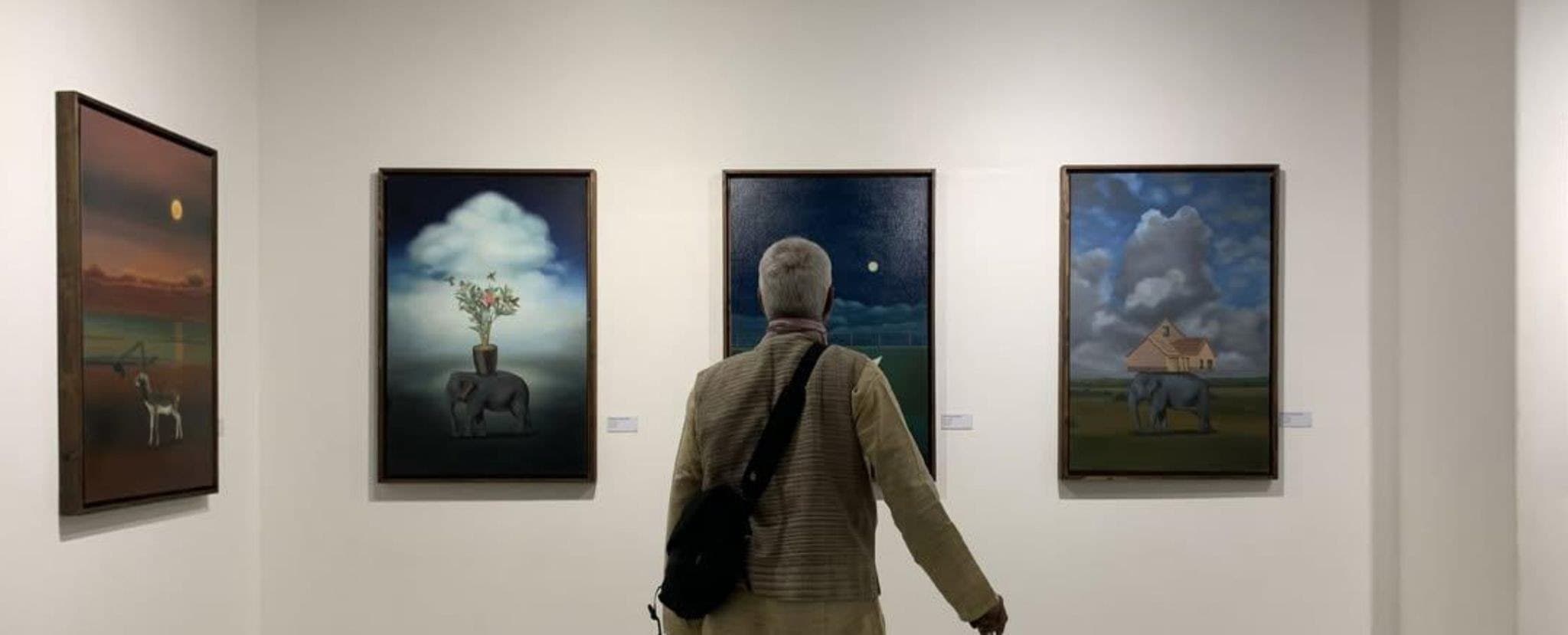 A visitor with a walking stick standing before three paintings.