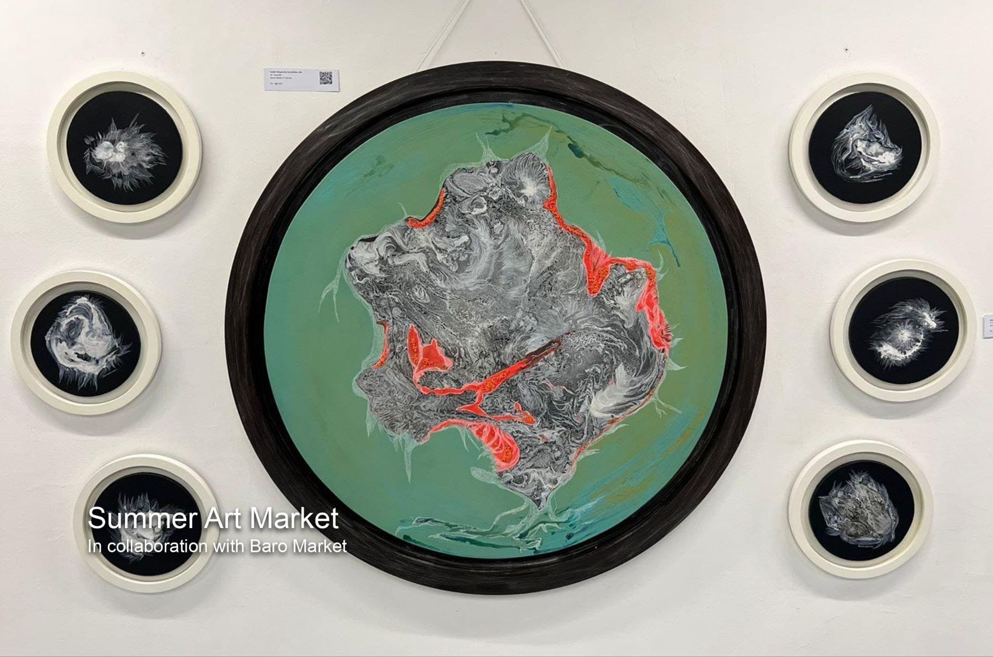 A large circular painting in green, grey and orange, surrounded by six smaller round works in white frames.